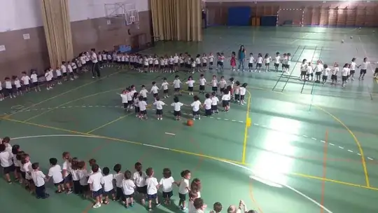 picture of a large hall in a school with children in a ring playing a game with a ball
